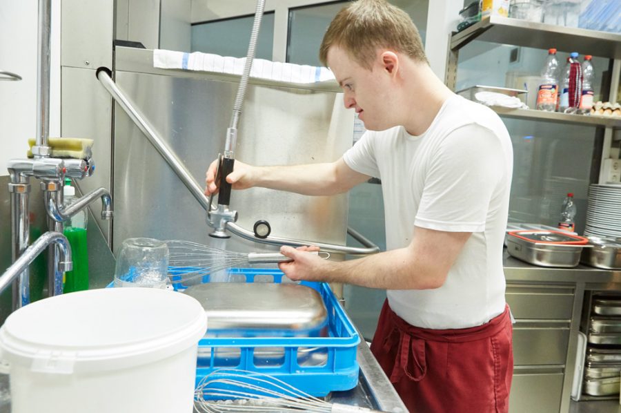 Der 27-jährige Florian spült in der Restaurantküche mit einer von der Decke hängenden Geschirrspülbrause einen Schneebesen ab.