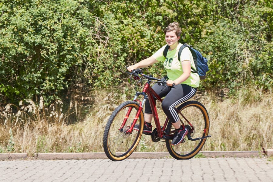 Tamara in voller Fahrt auf ihrem roten Mountainbike. Lächelnd genießt sie die Schräglage ihres Fahrrads. Im Hintergrund grünes Buschwerk.